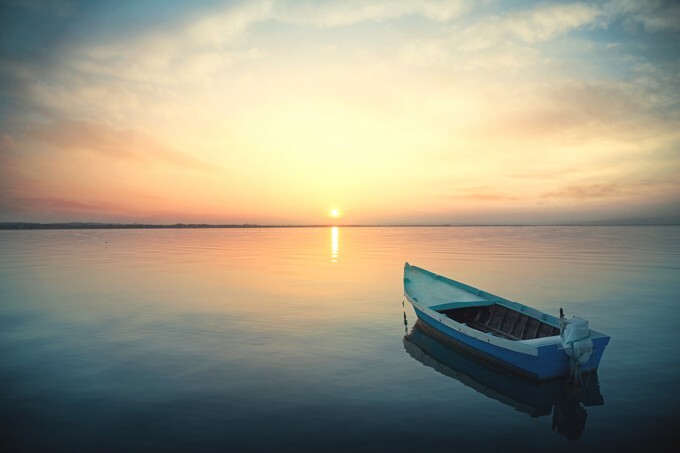 Small boat floating on the calm water under amazing sunset